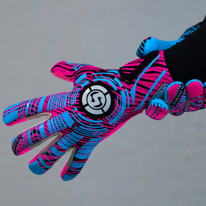 A close-up of a goalkeeper glove worn on a hand, featuring a vibrant neon pink and blue pattern with black accents and a circular logo on the back of the hand.