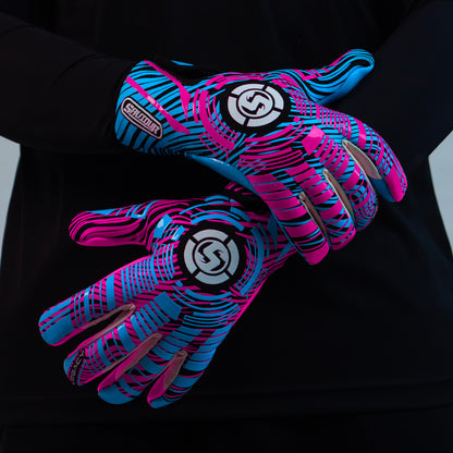 A pair of goalkeeper gloves with a vibrant pink and blue abstract pattern, worn on a person's hands against a black long-sleeve shirt.
