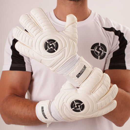 A person wearing white goalkeeper gloves with black circular logo details and the brand name 'SAVIOUR' on the wrist straps, posed in front of a white and black athletic soccer jersey.