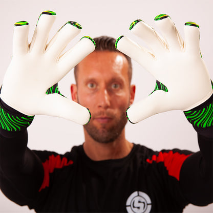 A man wearing white goalkeeper gloves with green accents, holding his hands up in front of his face against a plain light background.