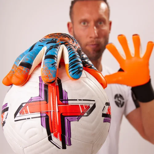 Goalkeeper catching a football with vibrant orange goalkeeper gloves during a match.