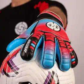 Goalkeeper catching a ball wearing blue and red soccer goalkeeper gloves.